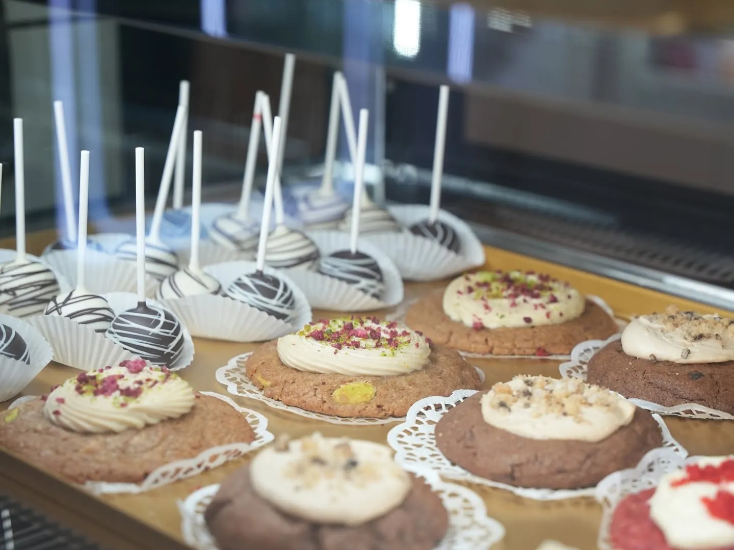 Cookies met roomtoef en cakepops op gouden schalen in de vitrine van COMO
