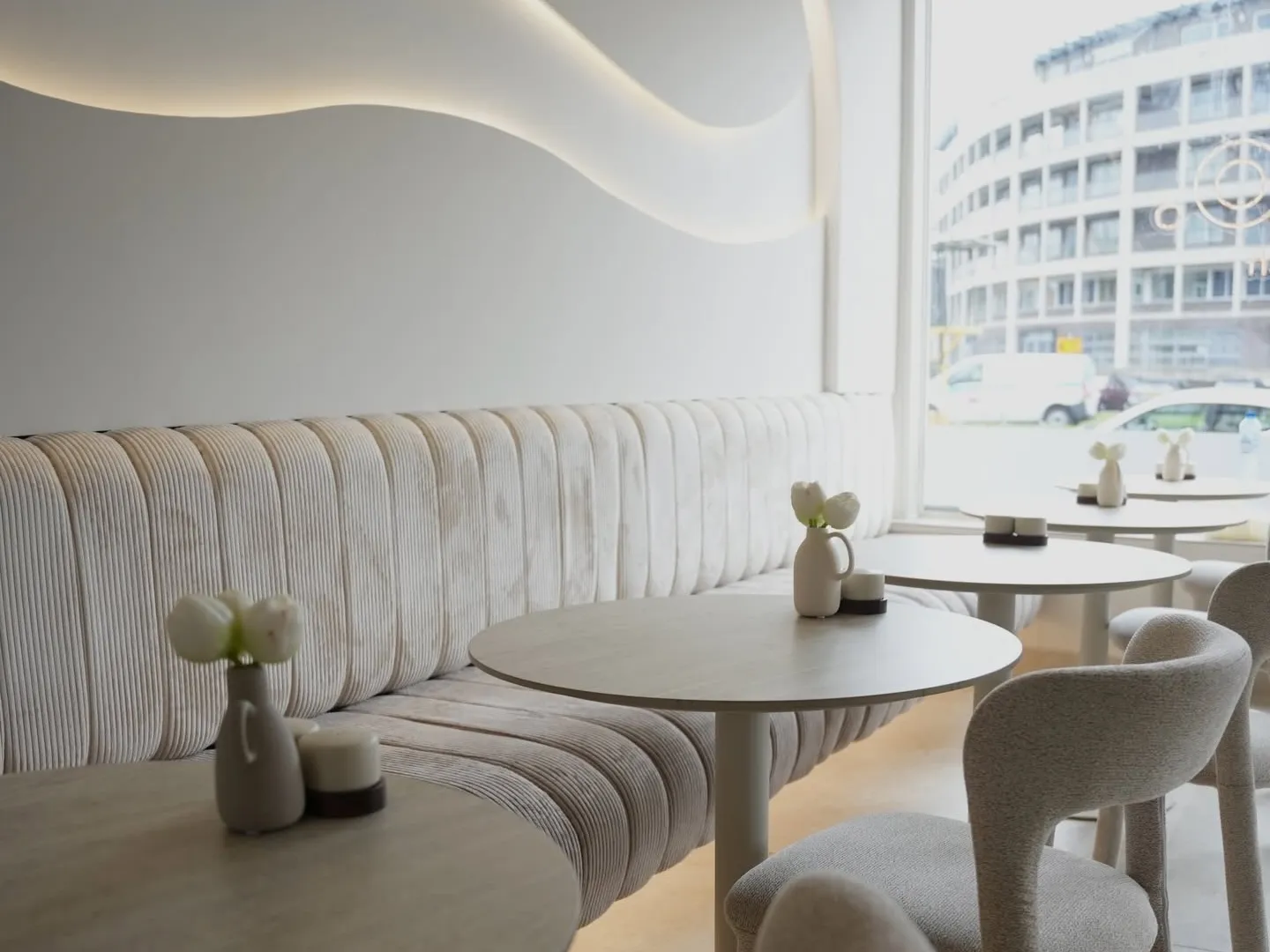 De zaal van COMO met de geribde crèmekleurige bank, ronde travertijnen tafels en het golvende lichtreliëf in het plafond