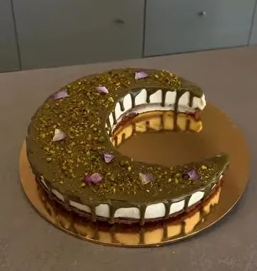 Een taart in de vorm van een letter met pistache en rozenblaadjes op een gouden schaal